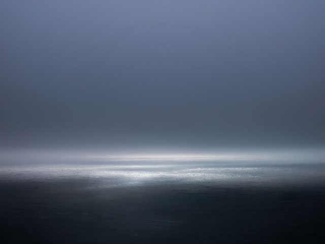 A photograph of a body of water with reflected light on the surface and a horizon line.
