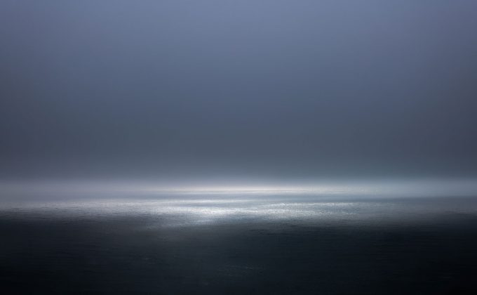 A photograph of a body of water with reflected light on the surface and a horizon line.