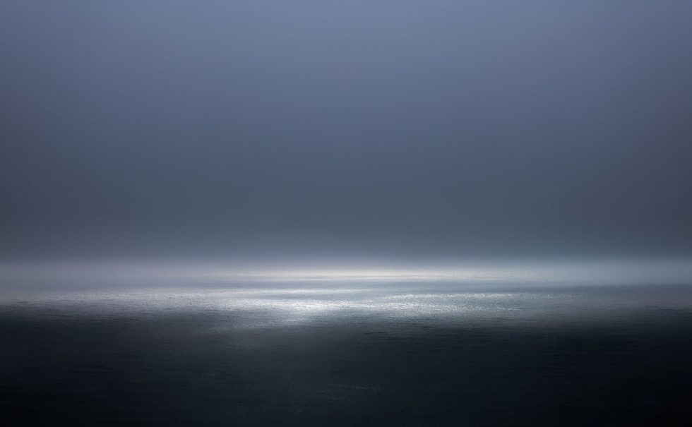A photograph of a body of water with reflected light on the surface and a horizon line.