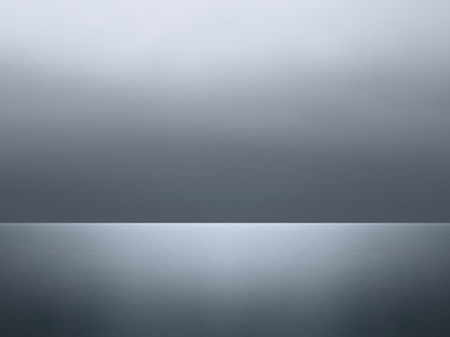 A photograph of a body of water with reflected light on the surface and a horizon line.