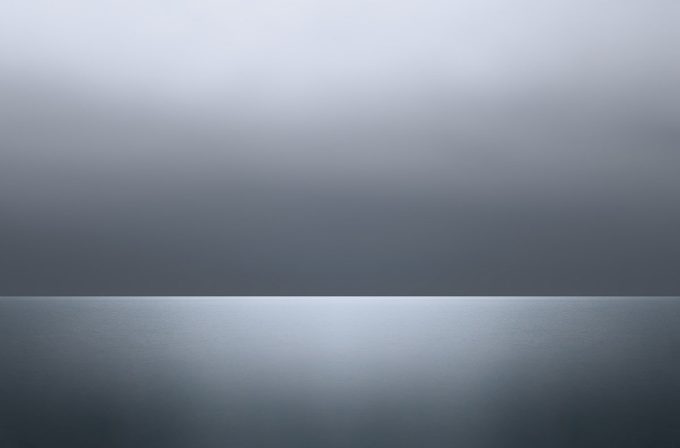 A photograph of a body of water with reflected light on the surface and a horizon line.