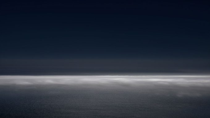 A photograph of a body of water with reflected light on the surface and a horizon line.