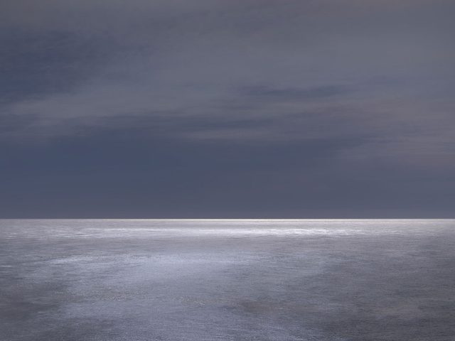 A photograph of a body of water with reflected light on the surface and a horizon line.