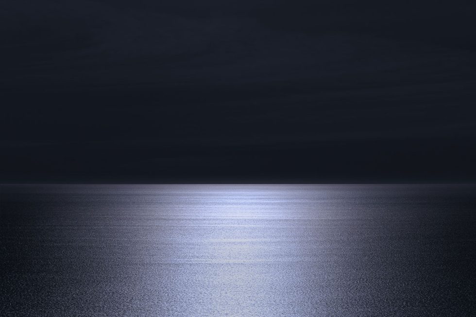 A photograph of a body of water with reflected light on the surface and a horizon line.