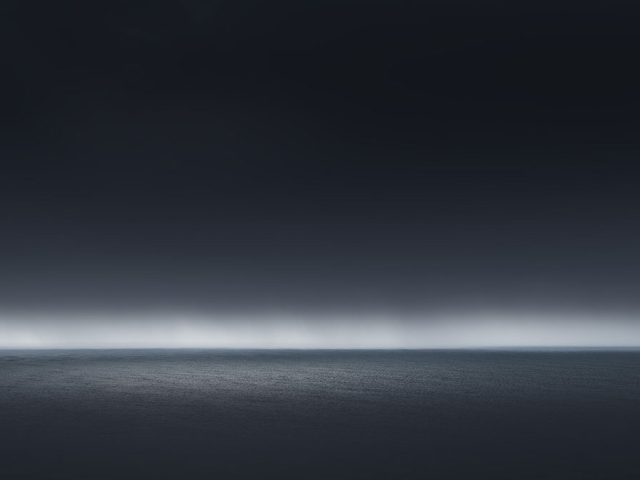 A photograph of a body of water with reflected light on the surface and a horizon line.