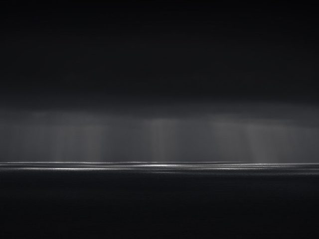 A photograph of a body of water with reflected light on the surface and a horizon line.