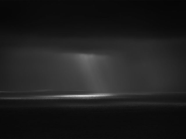A photograph of a body of water with reflected light on the surface and a horizon line.