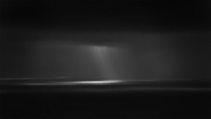 A photograph of a body of water with reflected light on the surface and a horizon line.
