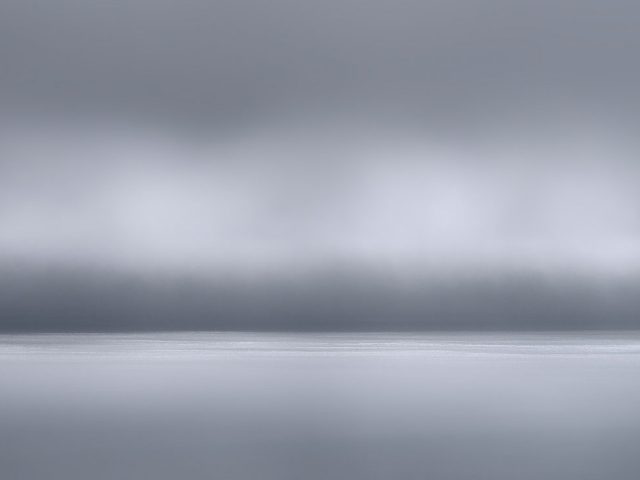 A photograph of a body of water with reflected light on the surface and a horizon line.