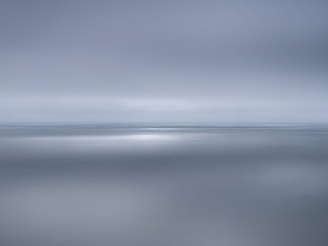 A photograph of a body of water with reflected light on the surface and a horizon line.