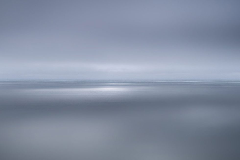 A photograph of a body of water with reflected light on the surface and a horizon line.