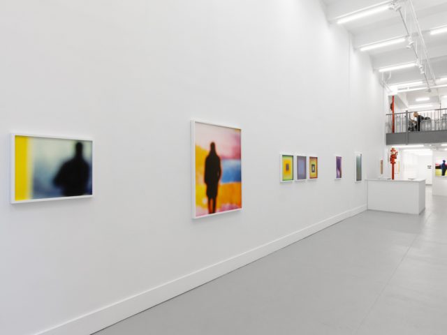 A photograph of an installation of colorful abstract works on a white gallery wall.