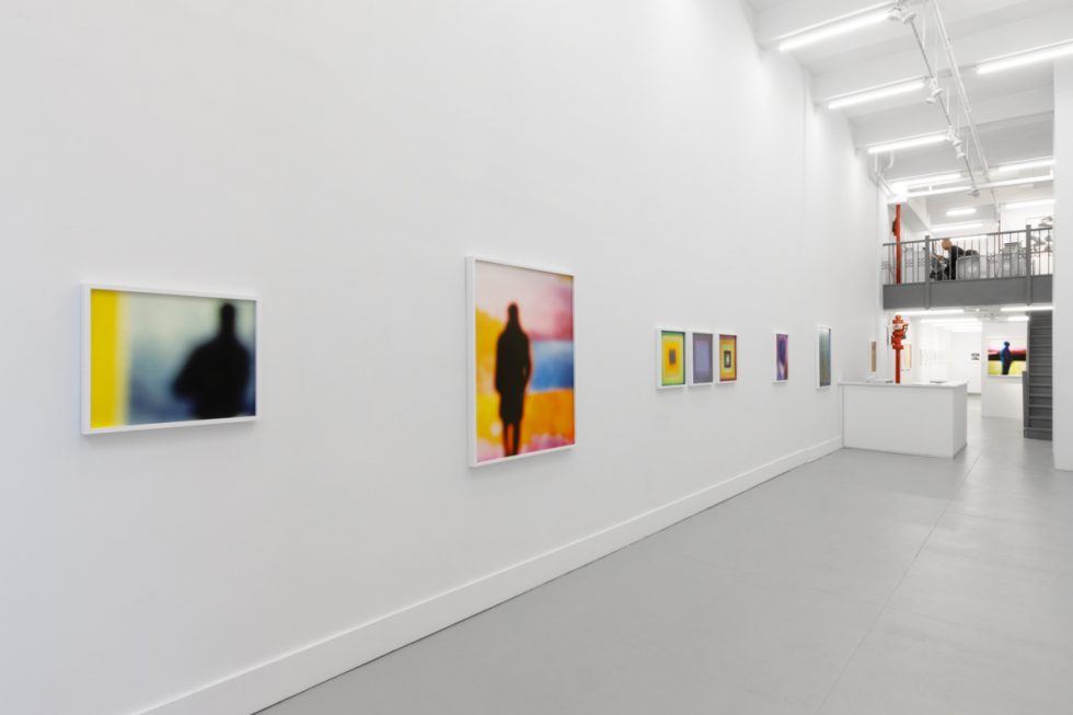 A photograph of an installation of colorful abstract works on a white gallery wall.