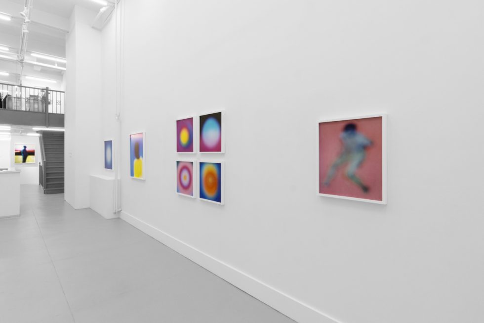 A photograph of an installation of colorful abstract works on a white gallery wall.