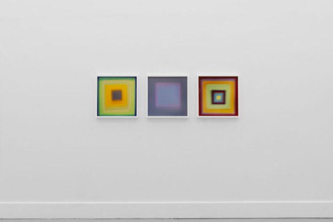 A photograph of an installation of colorful abstract works on a white gallery wall.