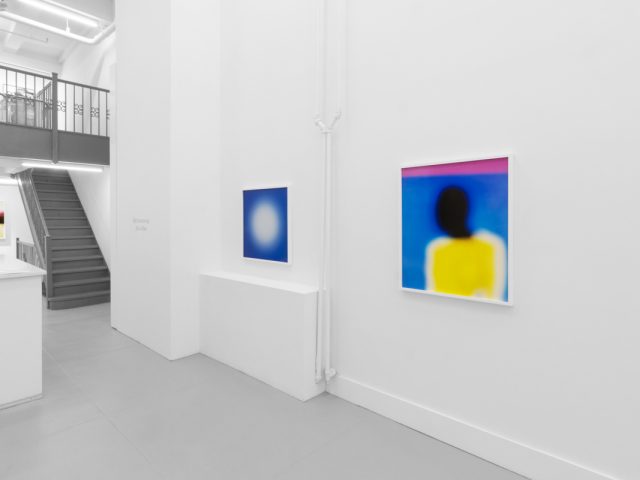 A photograph of an installation of colorful abstract works on a white gallery wall.