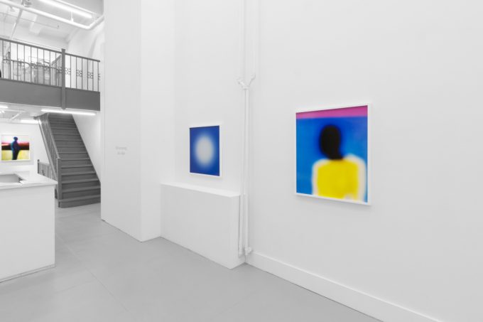 A photograph of an installation of colorful abstract works on a white gallery wall.