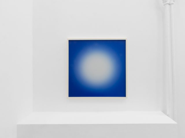 A photograph of an installation of colorful abstract works on a white gallery wall.