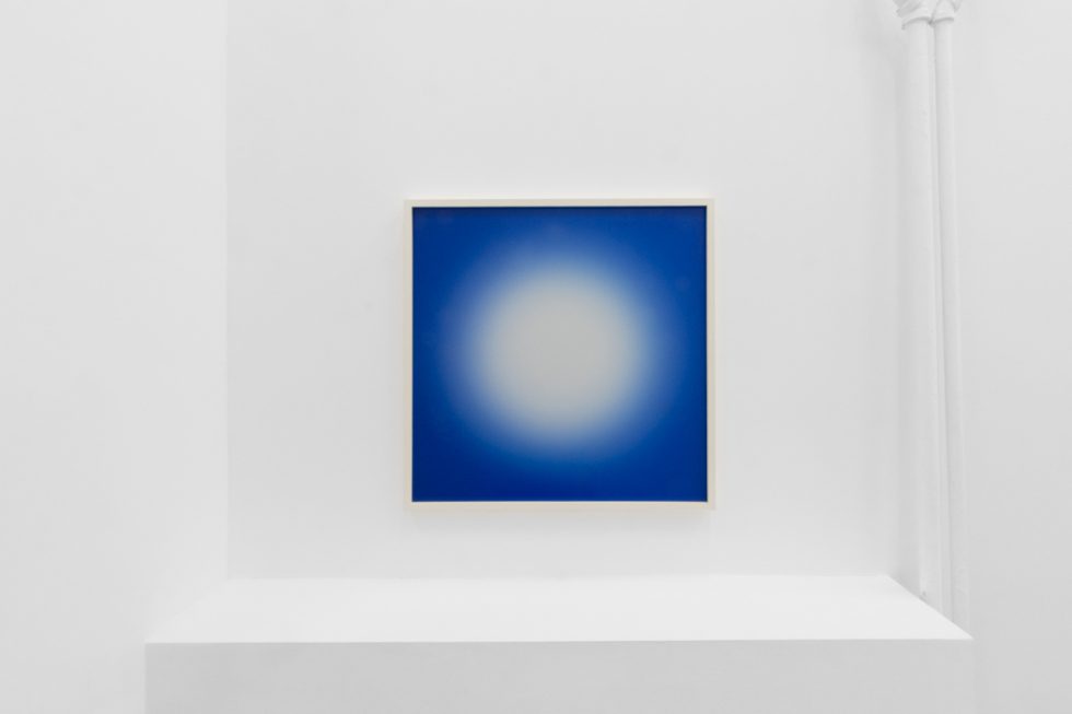 A photograph of an installation of colorful abstract works on a white gallery wall.