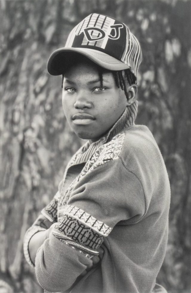 A black and white portrait of a young person in a cap with their arms crossed.