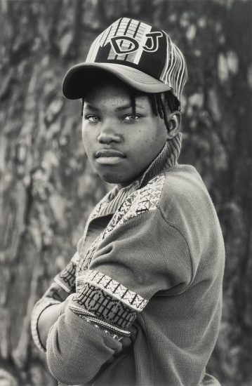 A black and white portrait of a young person in a cap with their arms crossed.