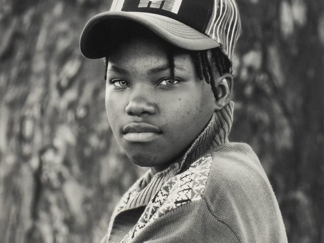 A black and white portrait of a young person in a cap with their arms crossed.