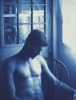 A cyanotype photograph of a shirtless man sitting in a chair by a window bathed in natural light.