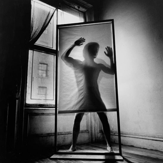 A black and white photograph of a shadow of a man being cast on a screen in an empty room.