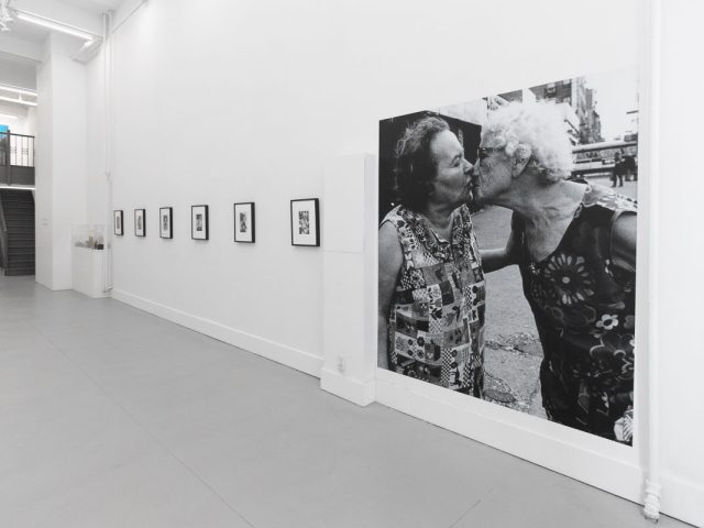 A photograph of a white-walled art gallery with black and white photographs with black frames on view.