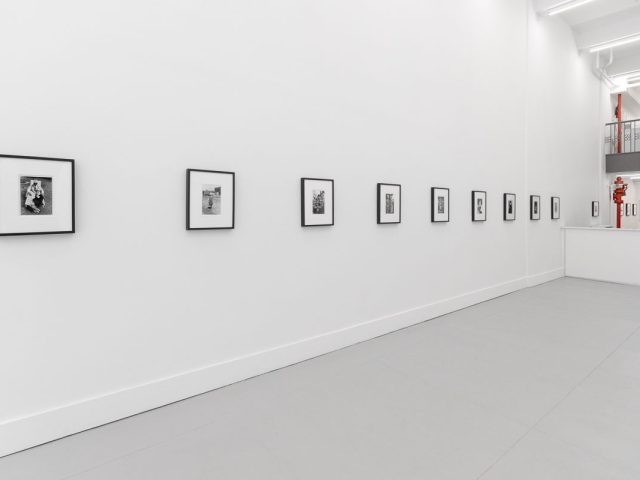 A photograph of a white-walled art gallery with black and white photographs with black frames on view.