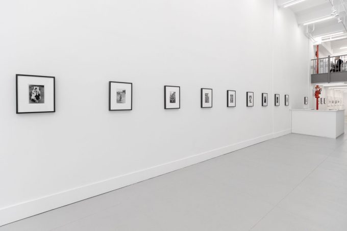 A photograph of a white-walled art gallery with black and white photographs with black frames on view.