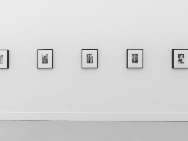 A photograph of a white-walled art gallery with black and white photographs with black frames on view.