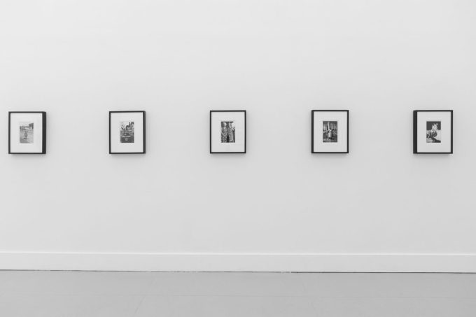 A photograph of a white-walled art gallery with black and white photographs with black frames on view.
