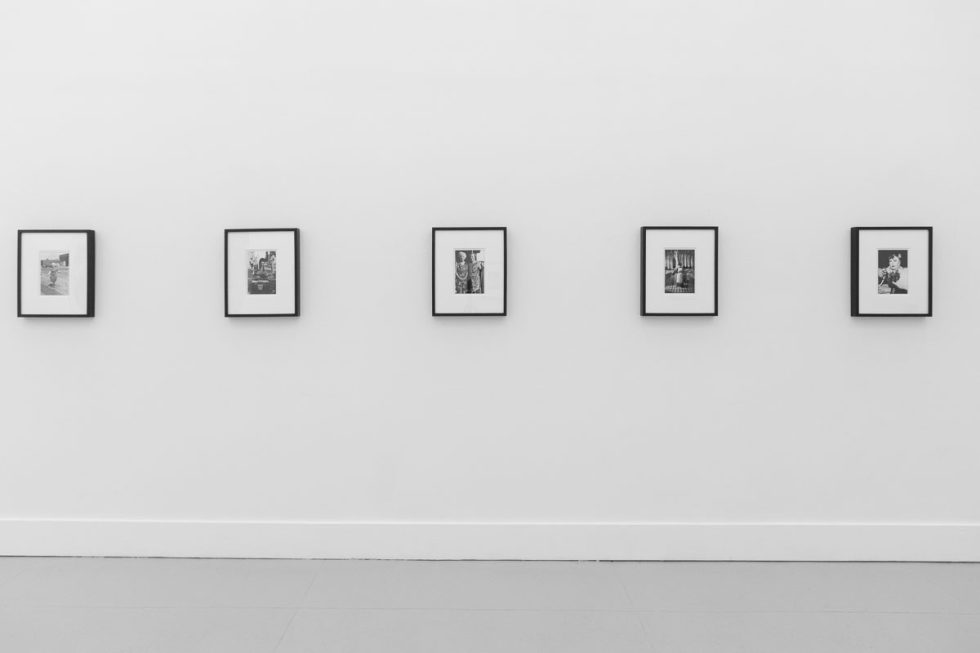 A photograph of a white-walled art gallery with black and white photographs with black frames on view.