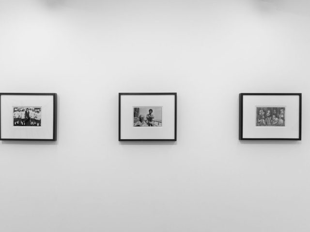 A photograph of a white-walled art gallery with black and white photographs with black frames on view.