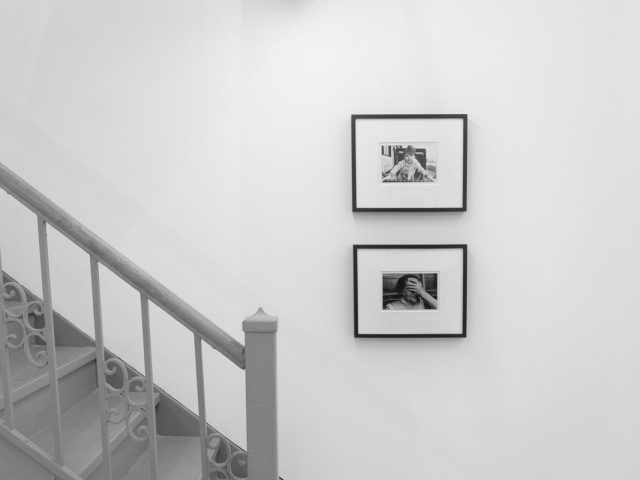A photograph of a white-walled art gallery with black and white photographs with black frames on view.