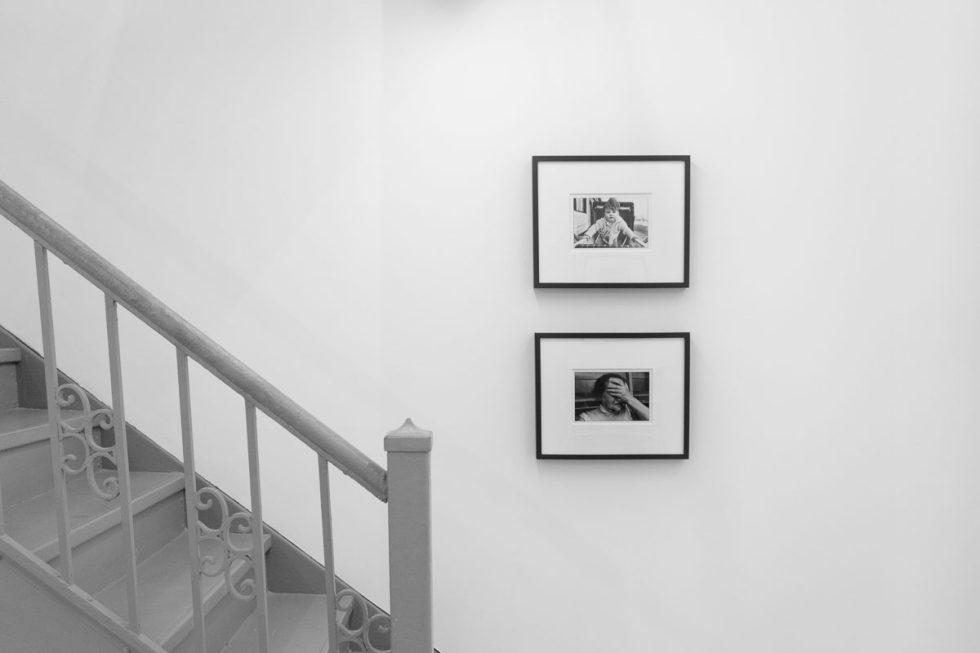 A photograph of a white-walled art gallery with black and white photographs with black frames on view.