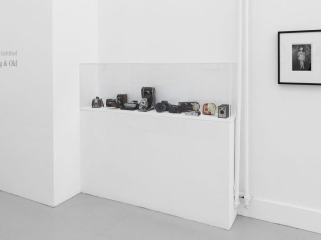 A photograph of a white-walled art gallery with black and white photographs with black frames on view.