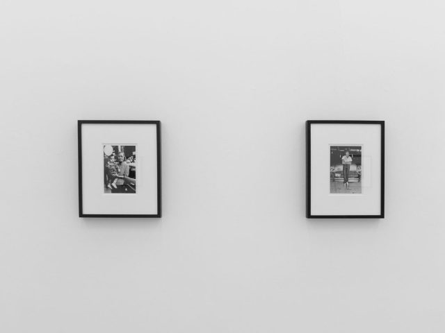 A photograph of a white-walled art gallery with black and white photographs with black frames on view.