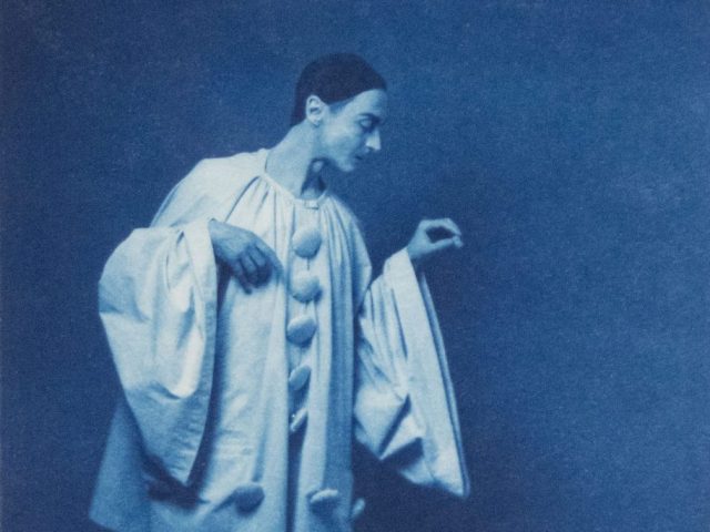 A cyanotype image of a circus performed with a bottle on the ground beside him.