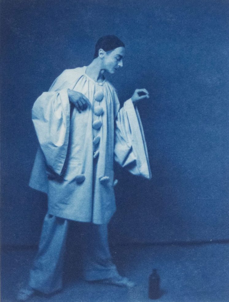 A cyanotype image of a circus performed with a bottle on the ground beside him.