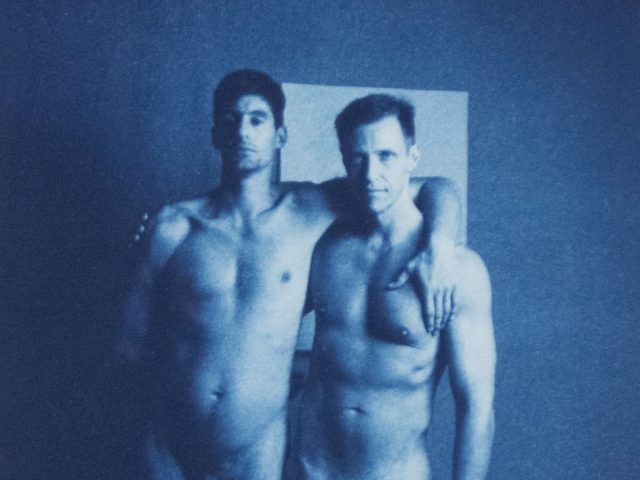 A cyanotype photograph of two nude men standing with their arms around each other's shoulders.