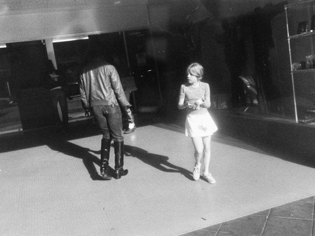 A black and white photograph of a girl in front of a storefront.