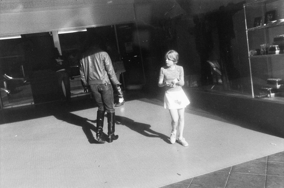 A black and white photograph of a girl in front of a storefront.