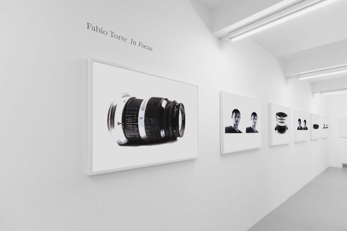 A photograph of a white-walled art gallery with black and white paintings with white frames on view.