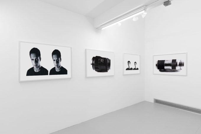 A photograph of a white-walled art gallery with black and white paintings with white frames on view.