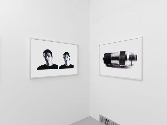 A photograph of a white-walled art gallery with black and white paintings with white frames on view.