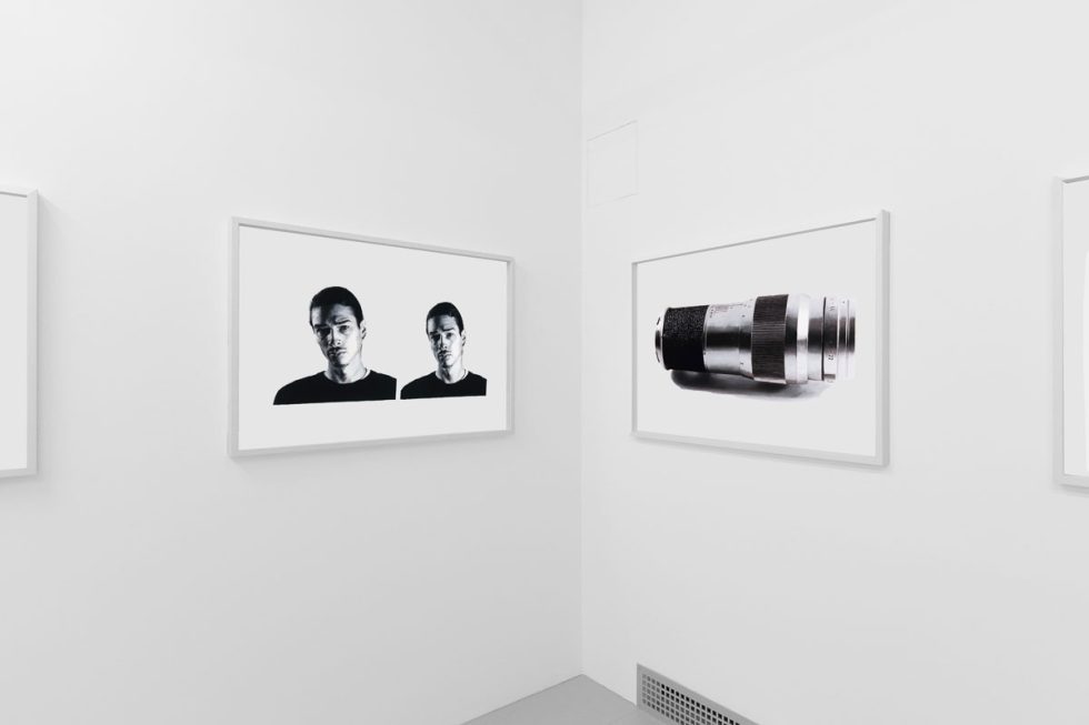 A photograph of a white-walled art gallery with black and white paintings with white frames on view.