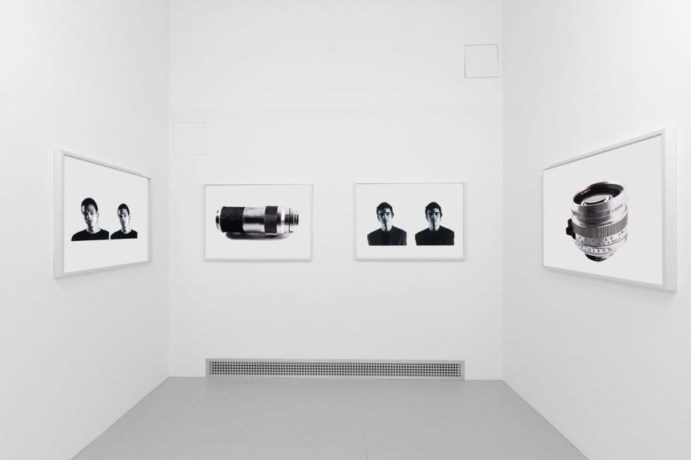A photograph of a white-walled art gallery with black and white paintings with white frames on view.