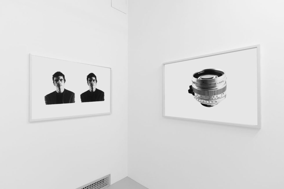 A photograph of a white-walled art gallery with black and white paintings with white frames on view.